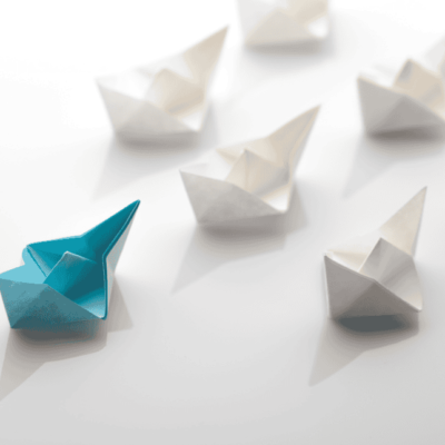 A blue origami boat leading multiple white origami boats