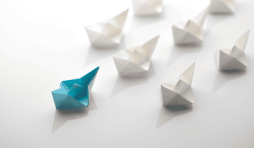 A blue origami boat leading multiple white origami boats